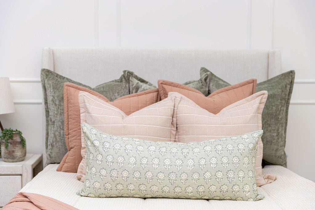 A close up view of a bed made with cream waffle textured zipper bedding and an assortment of green, pink, and floral pattern pillows and blanket.