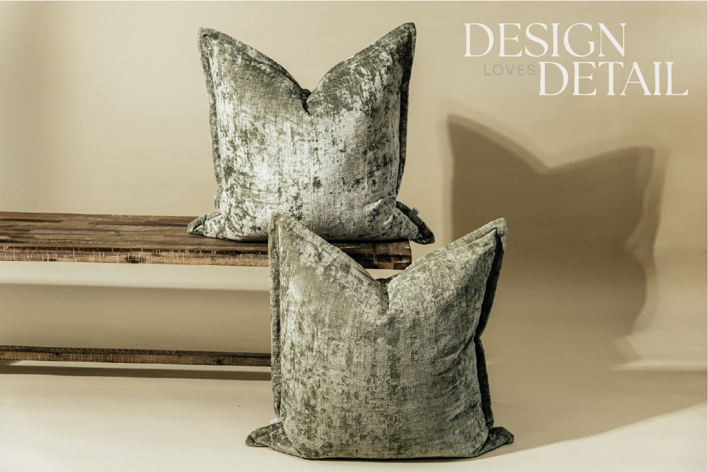 Two sage velvet green XL euro pillows on a bench and on the ground while arranged on a light green background.