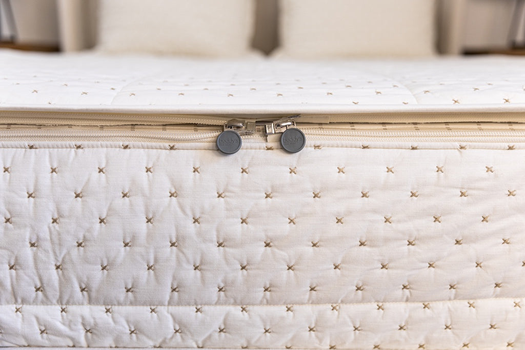 Close up photo of zipper being pulled on cream stitched X zipper bedding.