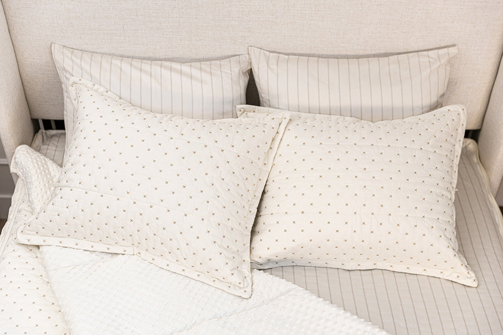 A bed made with cream embroidered zipper bedding with the comforter pulled back and pillows on top of the bed.