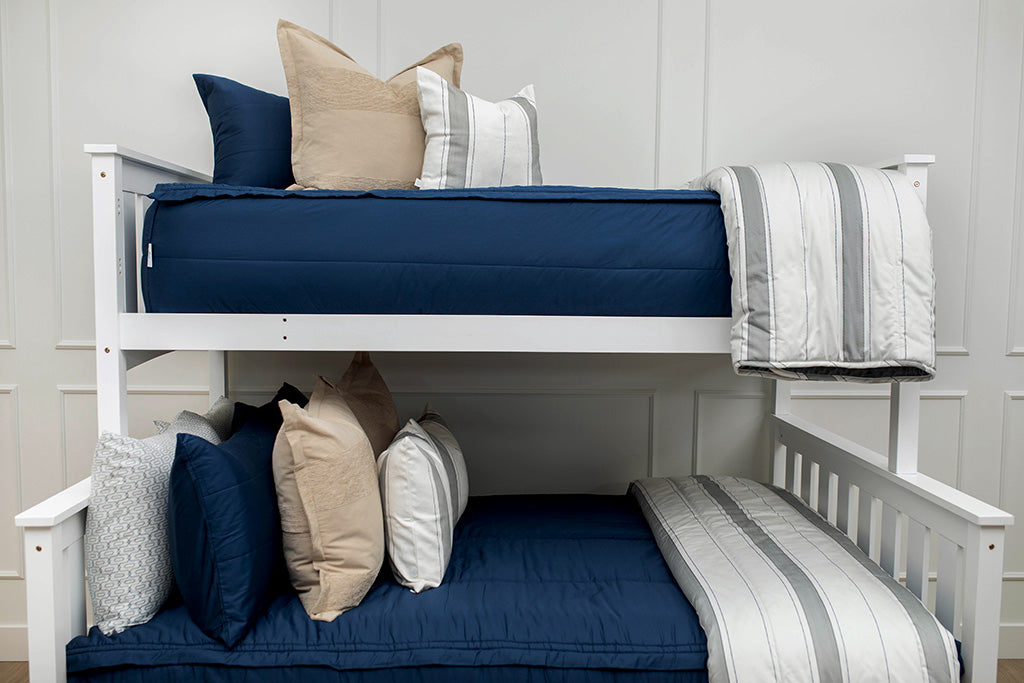 A standard bunk bed with both bunks made with navy blue zipper bedding and neutral and gray striped pillows and blankets.