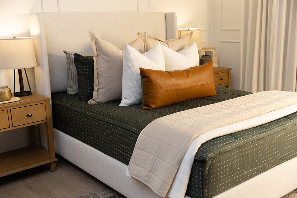 Queen bed with dark green zipper bedding with small cross design paired with tan, cream and brown pillows and blankets.