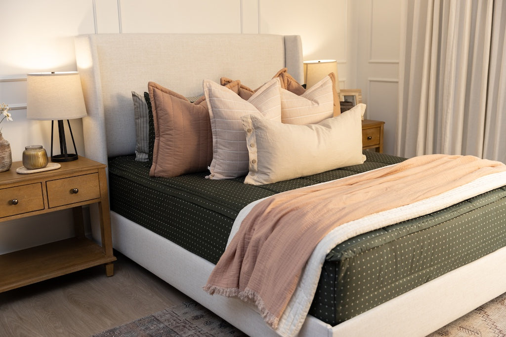 Queen bed with dark green zipper bedding with small cross design paired with terracotta, pink and tan pillows and blankets