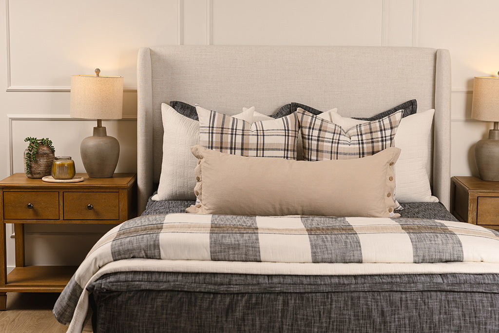 A close up view of a bed made with dark charcoal gray zipper bedding and leather and neutral striped pillows and blanket.