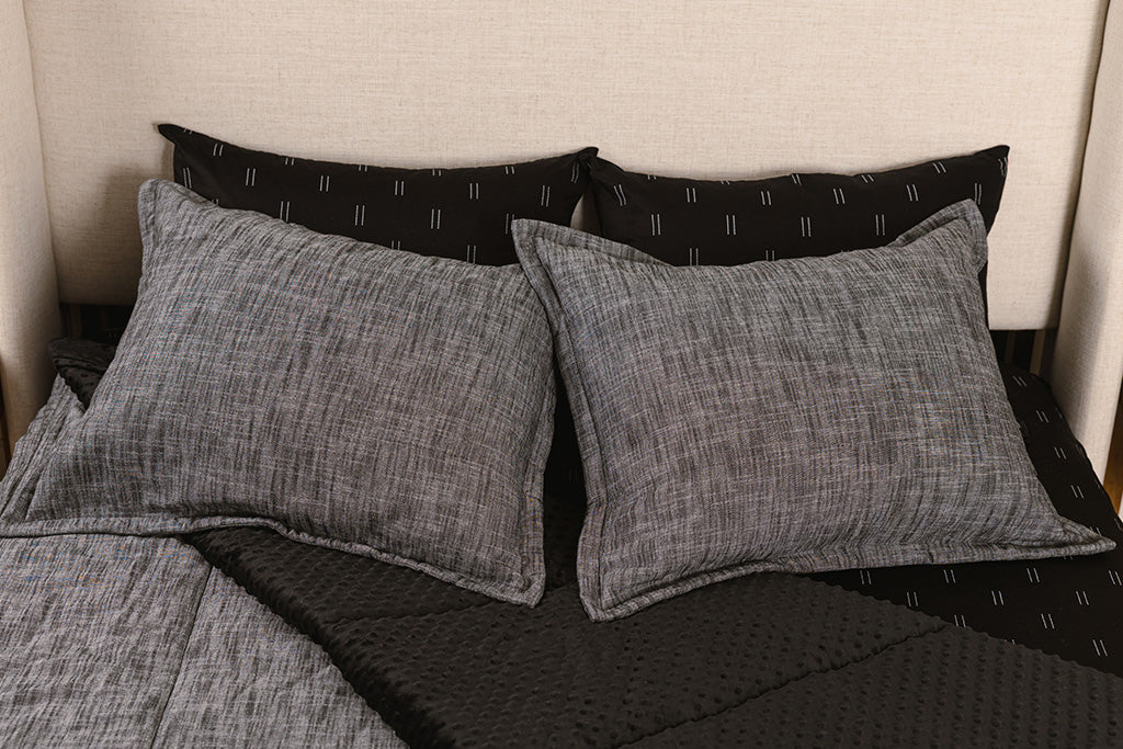 A bed made with dark charcoal gray zipper bedding with the comforter pulled back and pillows on top of the bed.