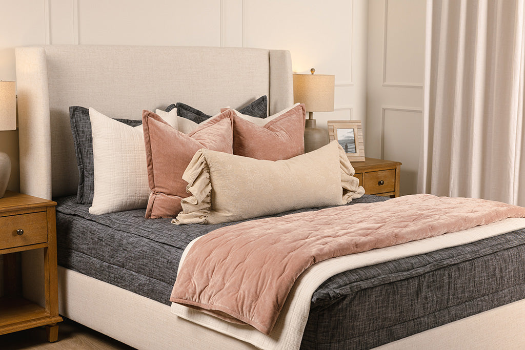 A queen bed made with dark charcoal gray zipper bedding and an assortment of pink and neutral pillows and blankets.