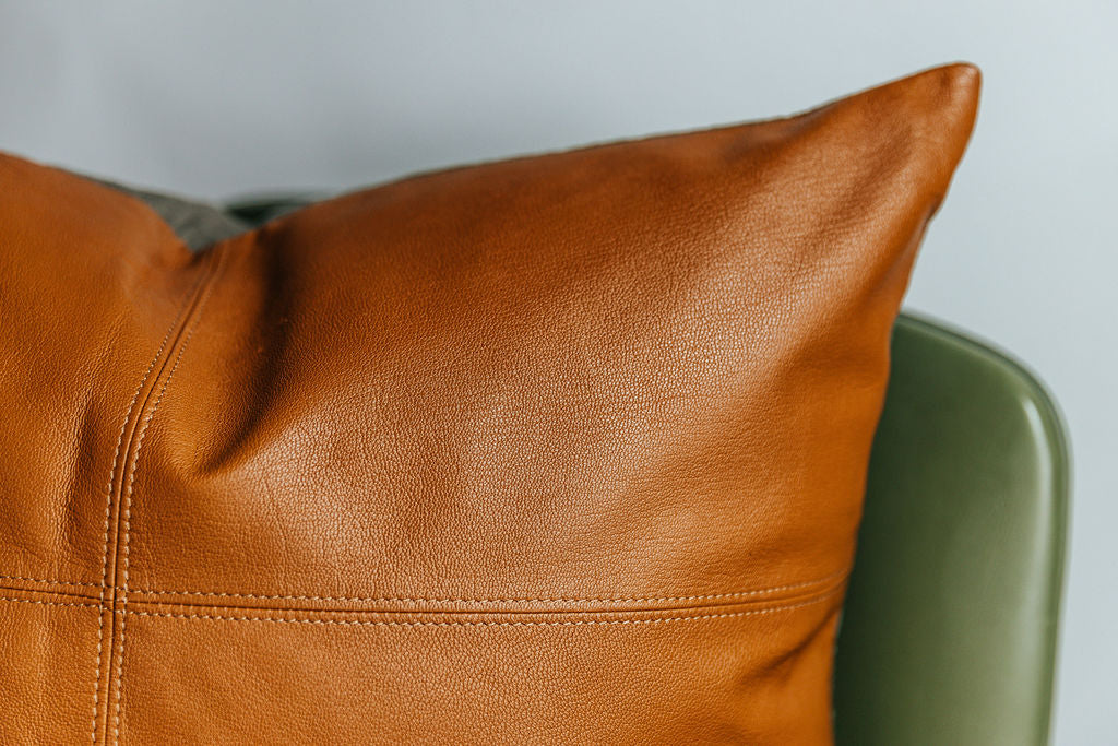 A close up view of a neutral leather euro pillow with stitching arranged on a chair.