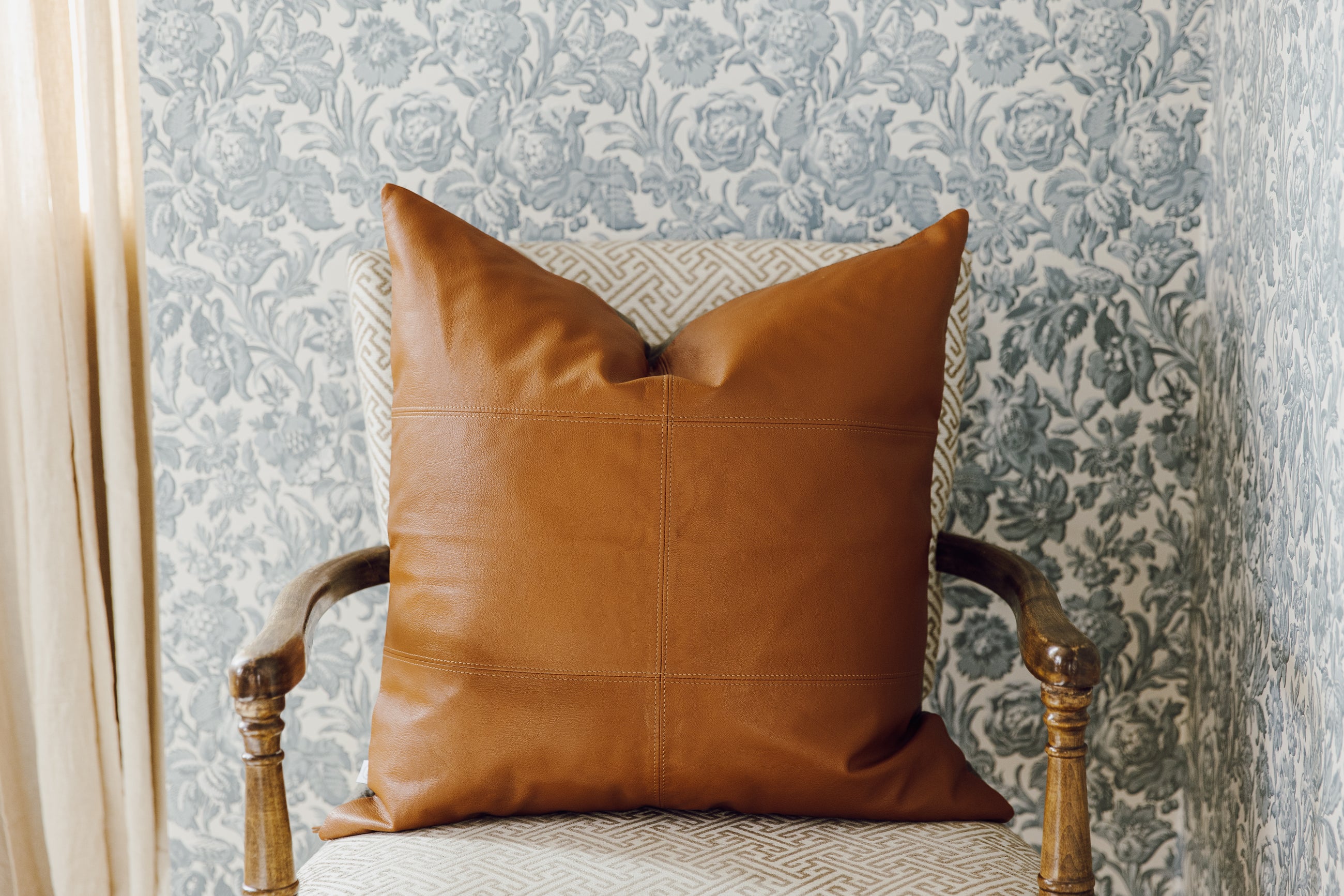 A neutral leather euro pillow with stitching arranged on a chair.