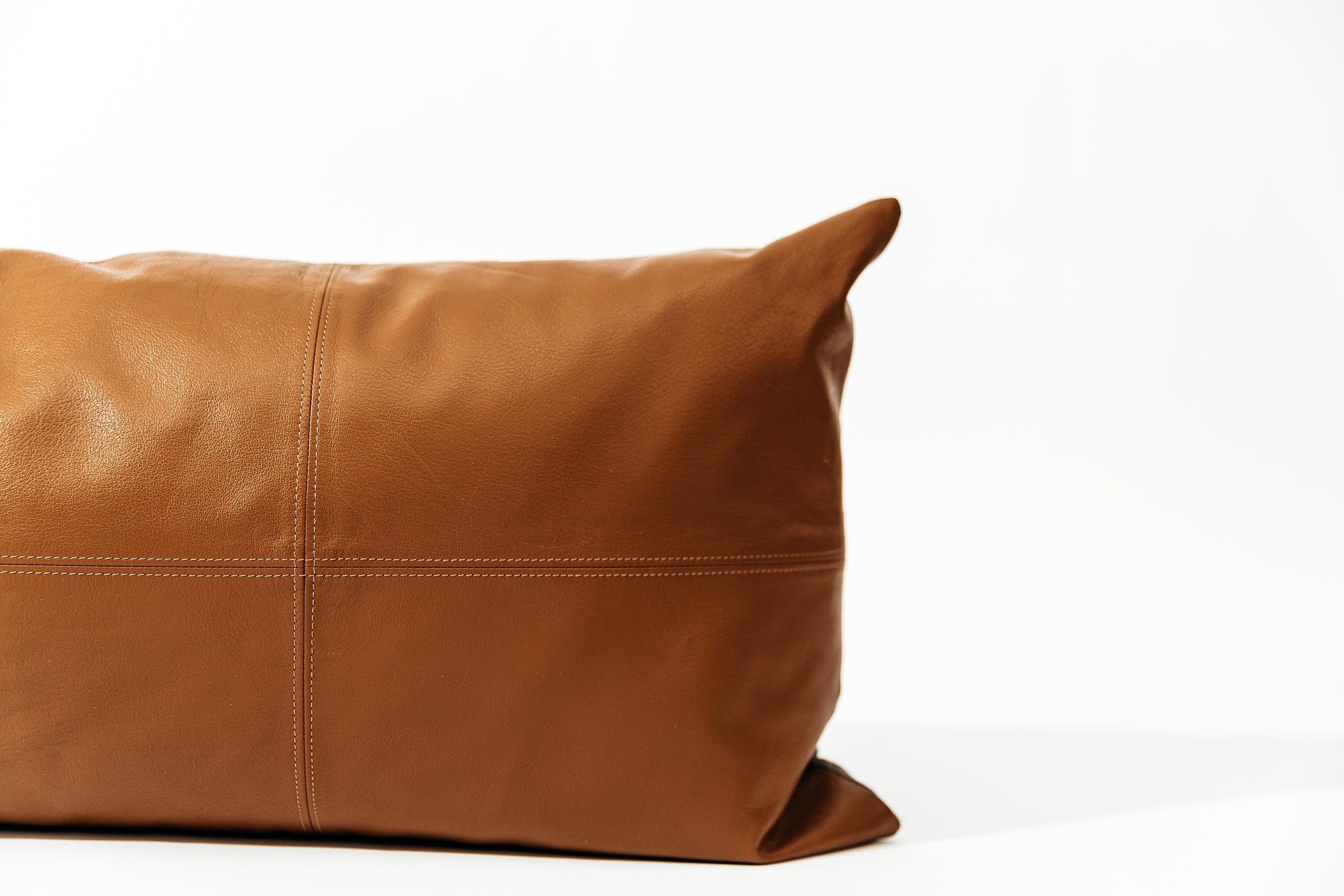 A close up view of a neutral leather XL lumbar pillow with stitching on a white background.
