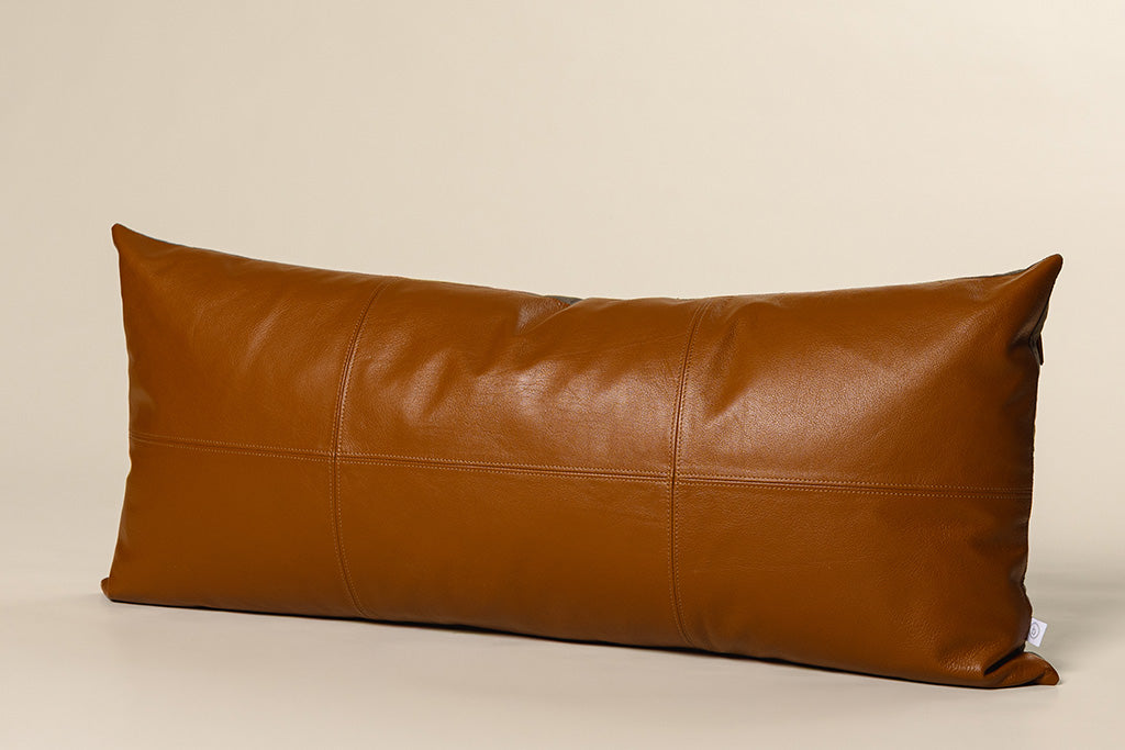 An orange brown leather pillow on a paper backdrop. 