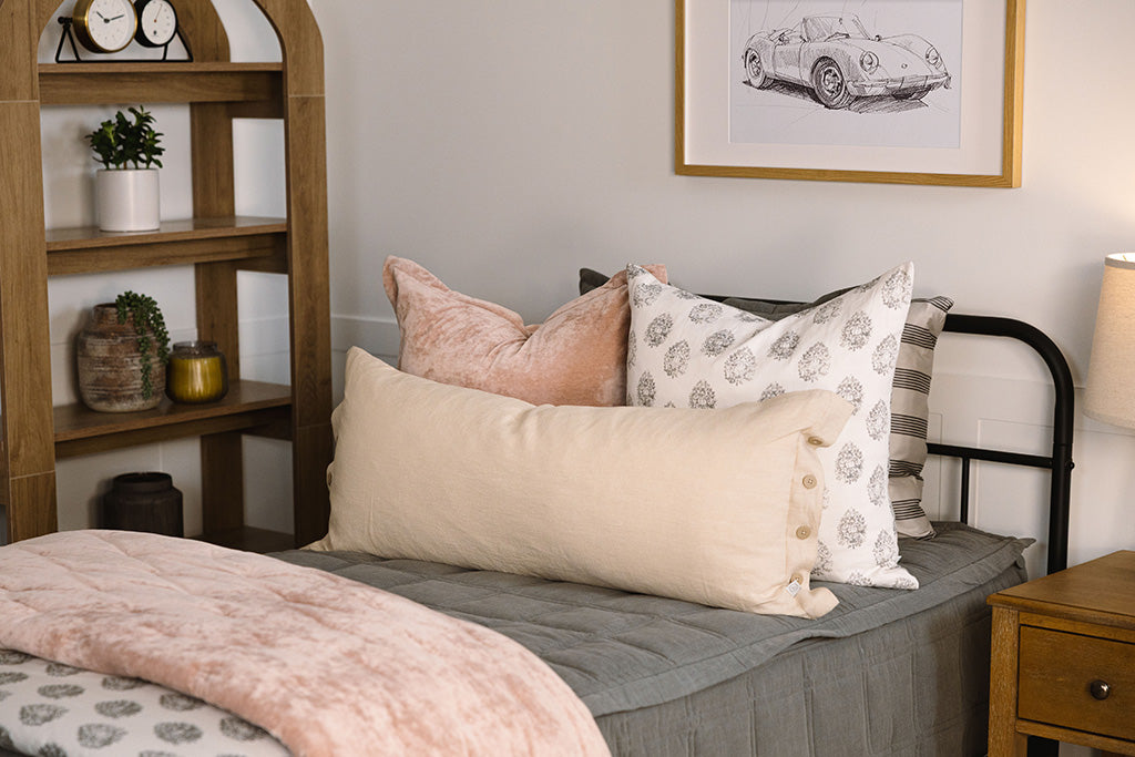 A twin bed made with gray zipper bedding and an assortment of floral and pink bedding accessories