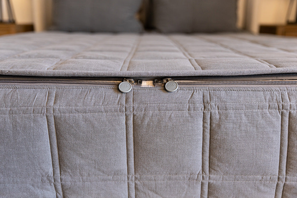 A shot of the foot of a bed made with gray zipper bedding with a focus on the 2 zippers