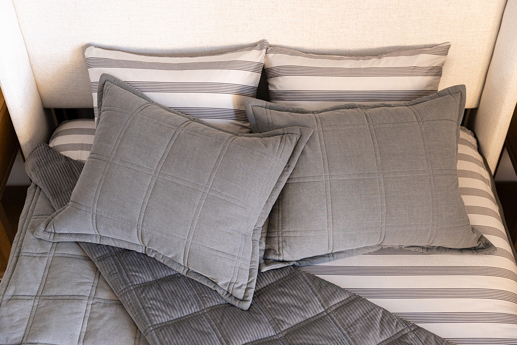 A bed made with gray zipper bedding with the top pulled back to reveal the inside lining, and four pillows arranged on top