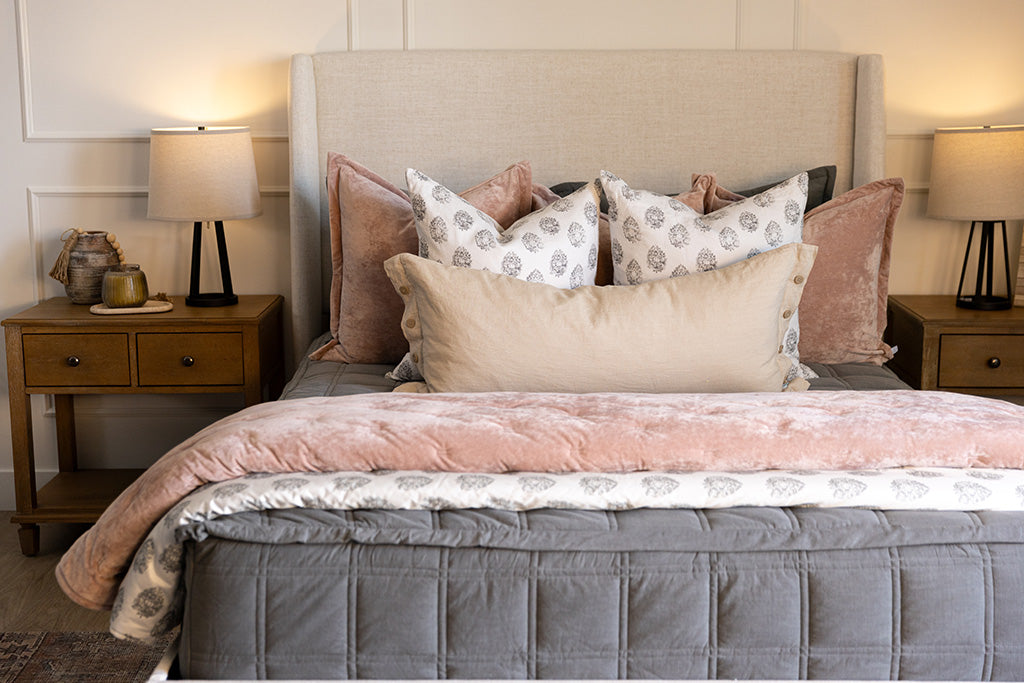A bed made with gray zipper bedding and an assortment of floral and pink bedding accessories