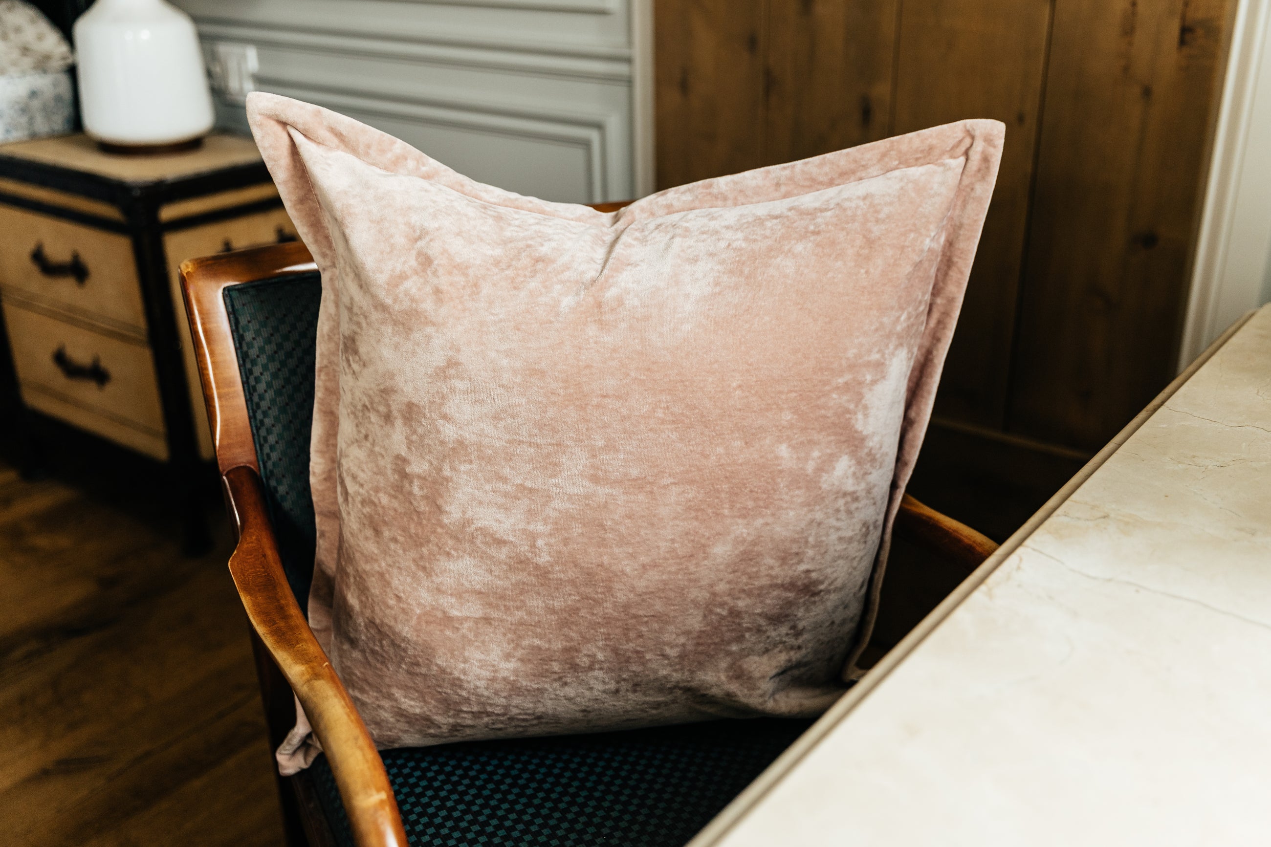 A pink velvet euro pillow arranged on a green antique chair by a desk.