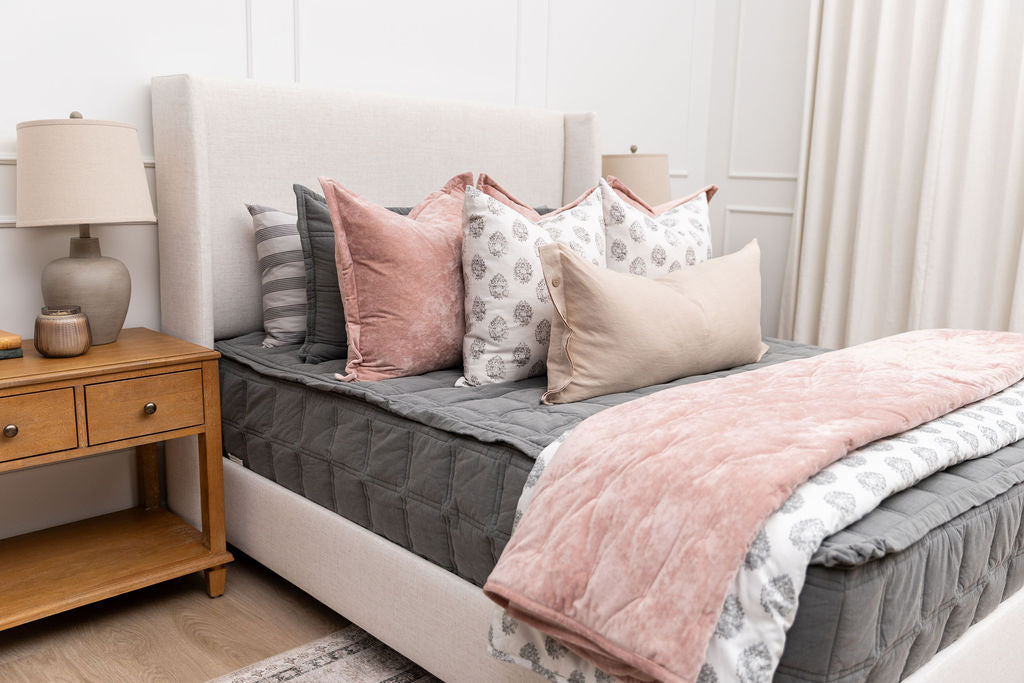 A bed made with gray zipper bedding and an arrangement of floral and pink velvet bed accessories.