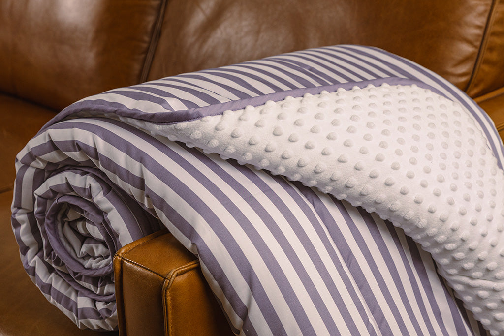 A purple and white striped blanket with white bubble minky on an orange leather couch. 