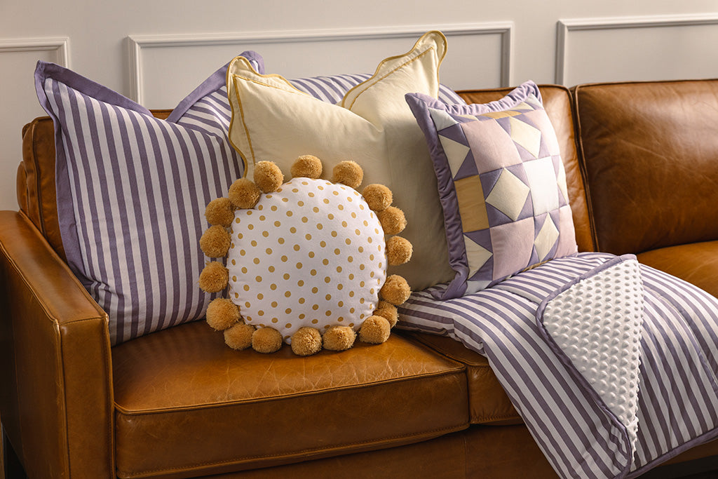 Purple, yellow, and white accessories on an orange leather couch.