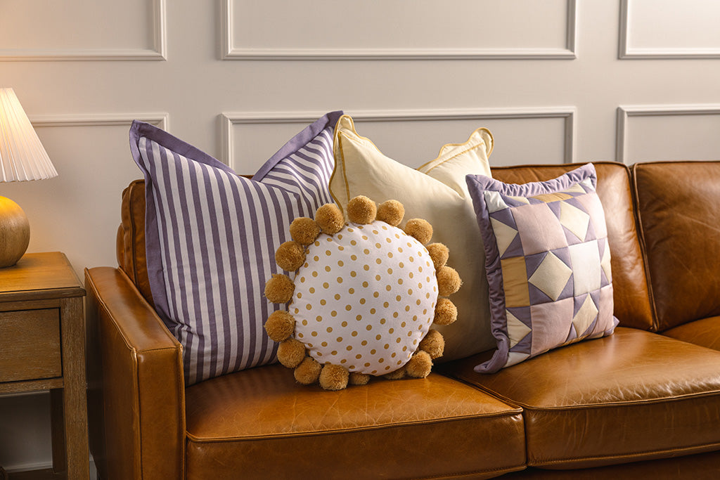 Purple, white, and yellow accessories on an orange leather couch. 