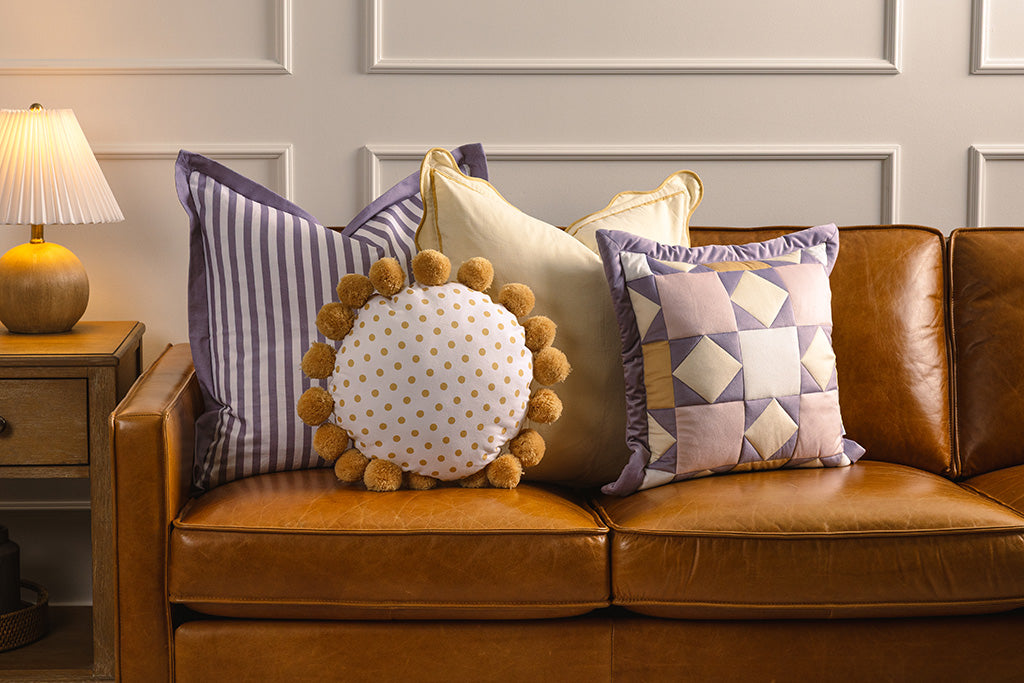 Purple, pink, cream, and yellow accessories on an orange leather couch.
