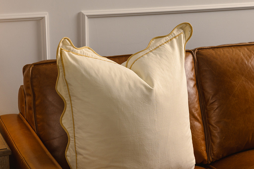 A yellow pillow on an orange leather couch.