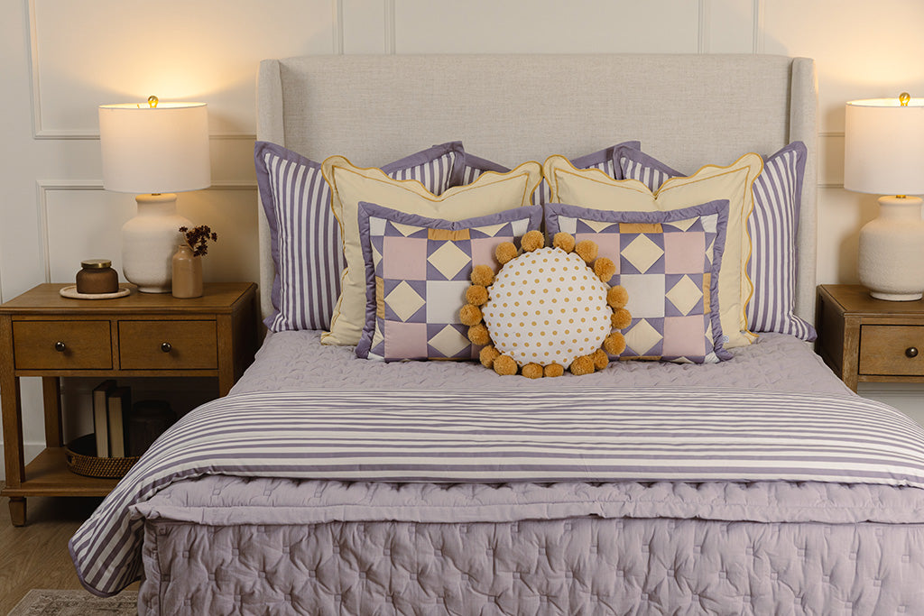 Purple puffed quilted bedding with yellow, purple, and white accessories. 