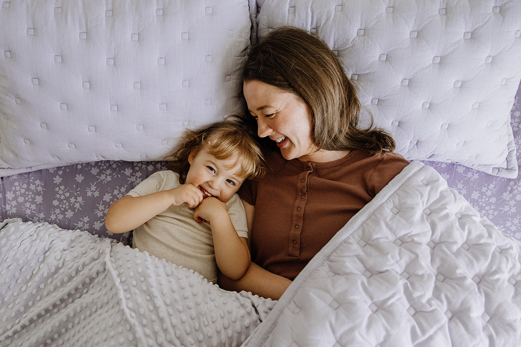 A mother and daughter snuggling in their purple puffed zipper bedding.