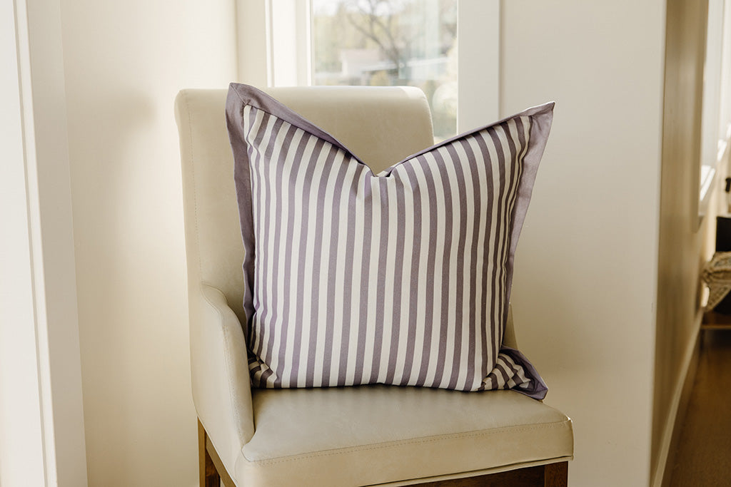 A purple and white striped pillow on a cream leather chair.