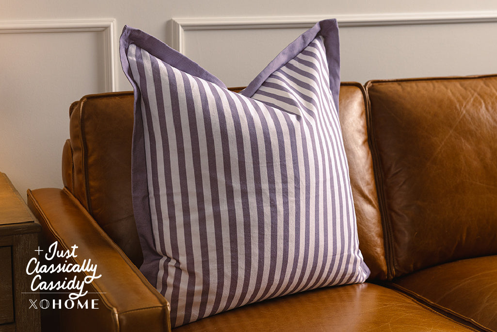 Purple and white striped pillow on an orange leather couch.