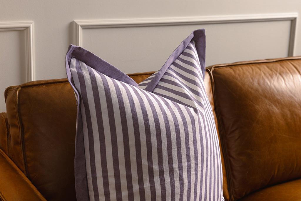 Purple and white striped pillow on an orange leather couch.
