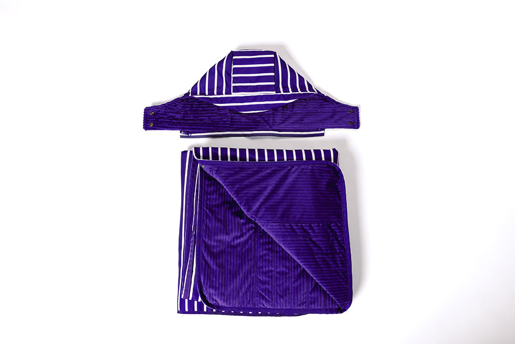 A purple and white striped stadium blanket and attachable hood folded on a white backdrop.
