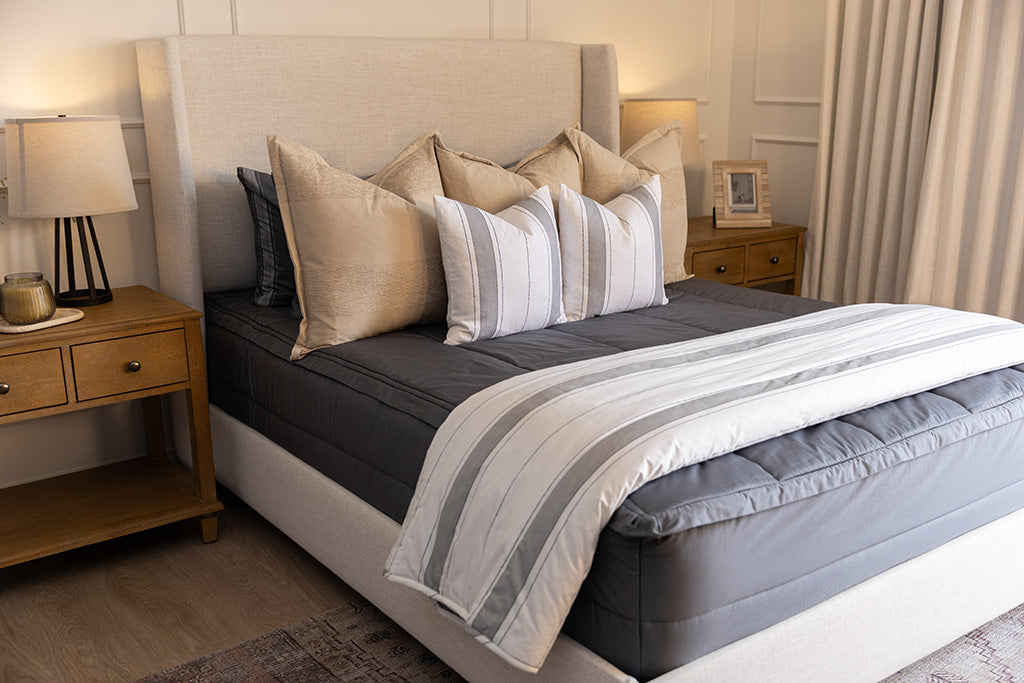 A bed made with gray zipper bedding and an assortment of neutral and striped throw pillows and blanket.