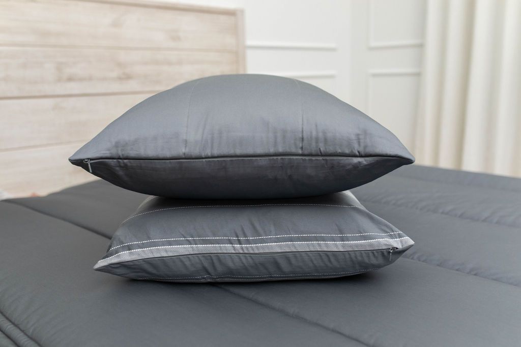 A gray zipper bedding made with an up close view of the matching pillows stacked in the middle of the bed. 