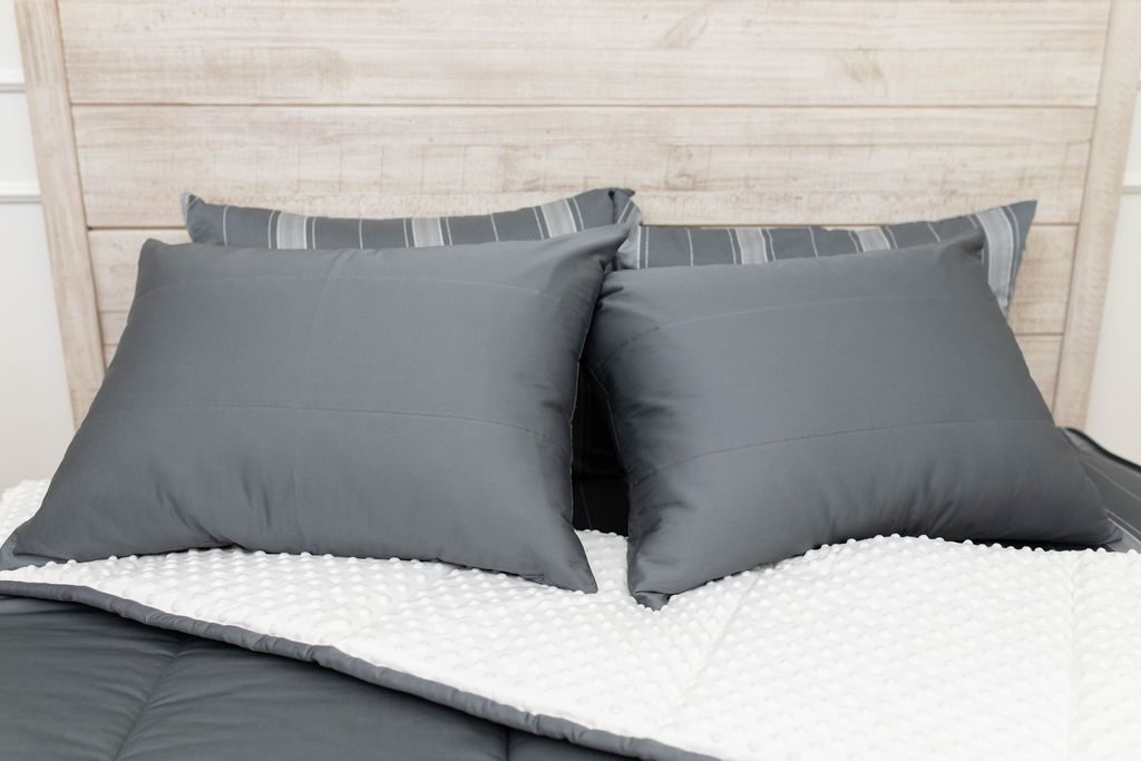 A bed made with gray zipper bedding with the comforter pulled back showing white minky lining and pillows on top of the bed.