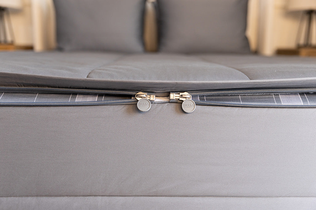 The foot of a bed made with gray zipper bedding showing where the two zippers are located.