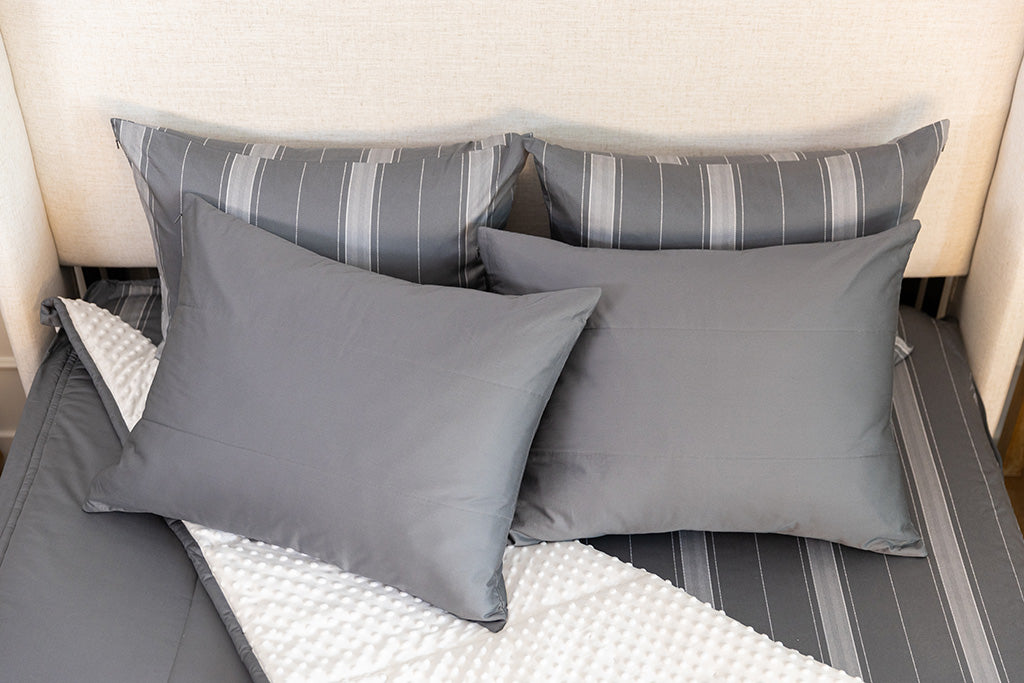 A bed made with gray zipper bedding with the comforter pulled back and pillows on top of the bed.