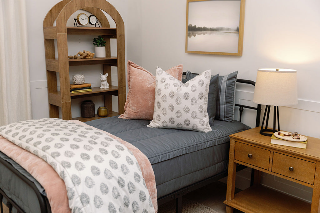 A queen bed made with gray zipper bedding and pink and gray floral pillows and blanket.