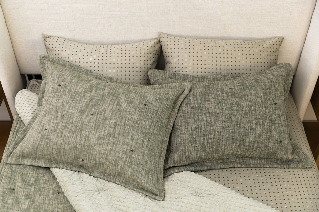 A bed made with deep emerald green zipper bedding with the comforter pulled back and pillows on top of the bed.
