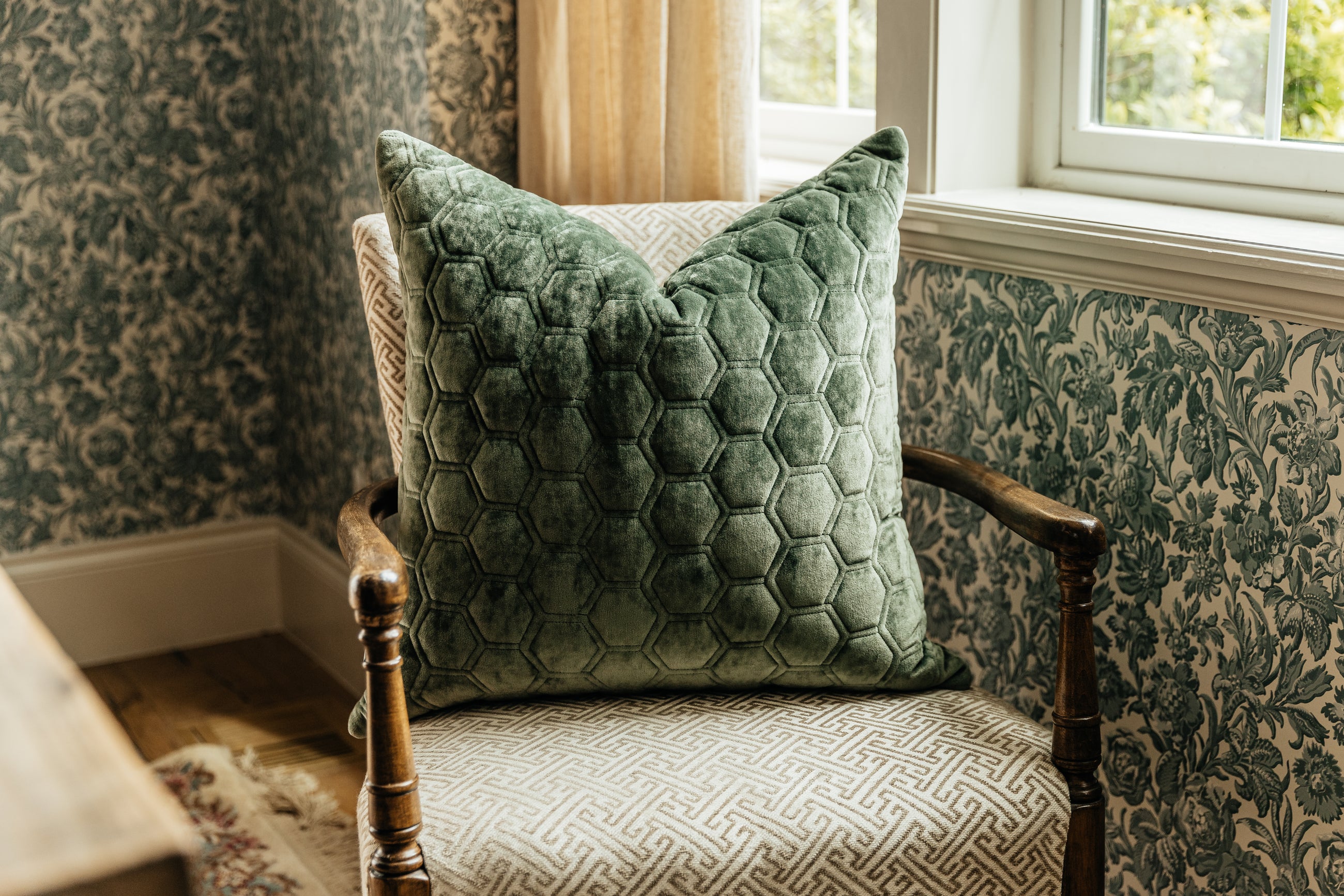 A green honeycomb pattern velvet euro pillow arranged on a chair next to a window.