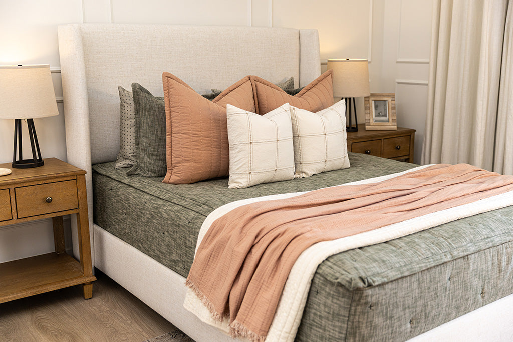 A queen bed made with deep emerald green zipper bedding and terracotta and neutral blankets and pillows.