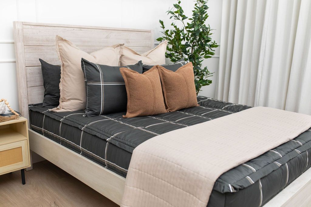 A bed made with charcoal, white, and brown grid pattern zipper bedding and tan and brown pillows and tan patterned blanket.