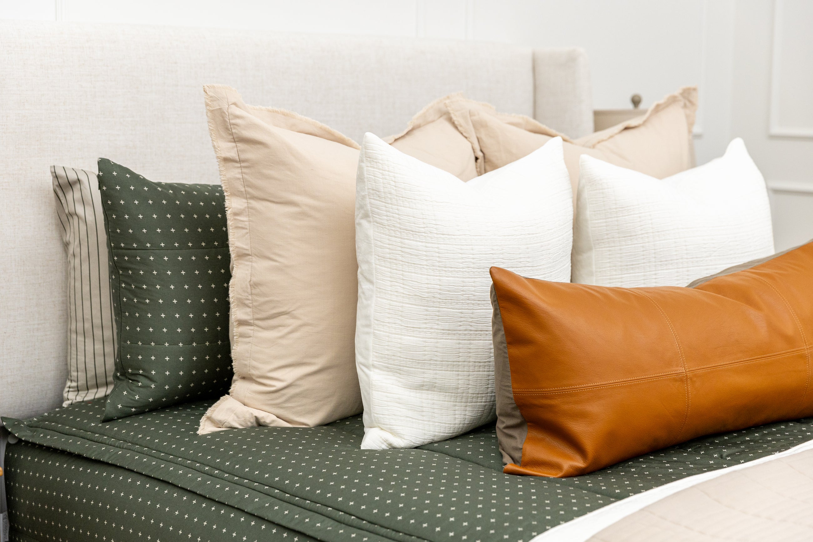 A bed made with dark green zipper bedding and an assortment of neutral tan, white, and leather pillows and blankets.