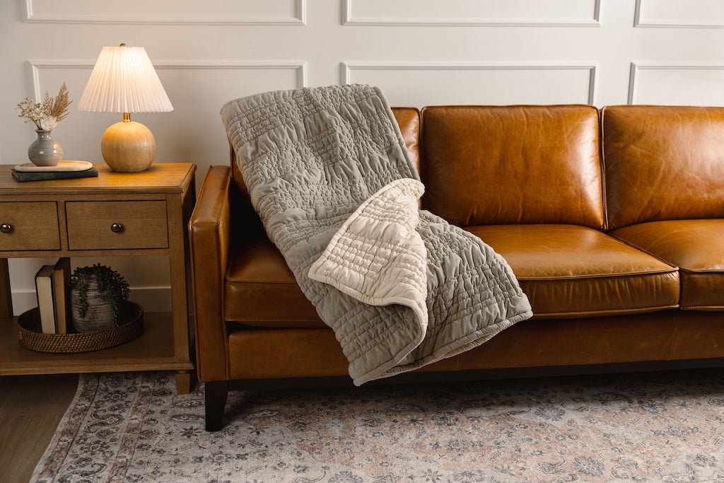 A sage green and cream blanket on an orange leather couch. 