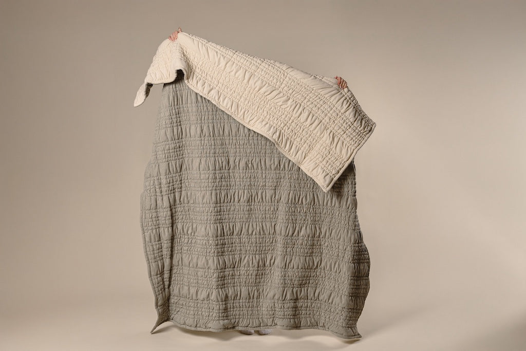 A model holding a sage green and cream scrunched blanket. 
