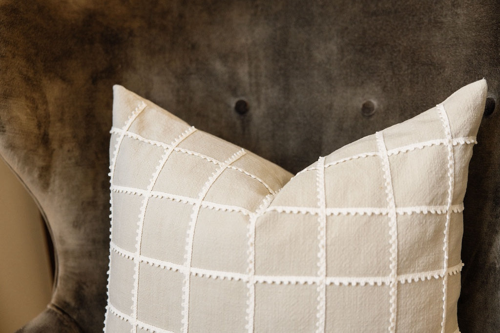 A tan and a cream trimmed grid pattern pillow on a velvet olive green chair.