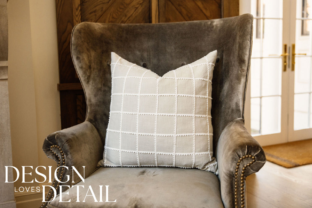 A tan and a cream trimmed grid pattern pillow on a velvet olive green chair.