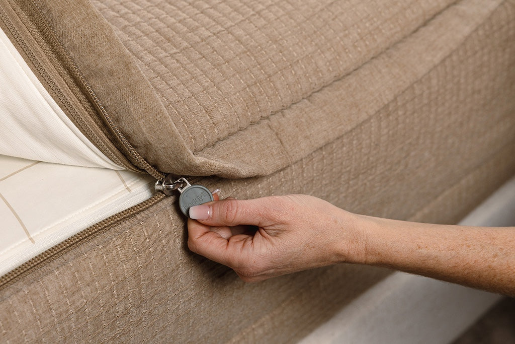 A close up photo of a zipper being pulled on tan woven zipper bedding.