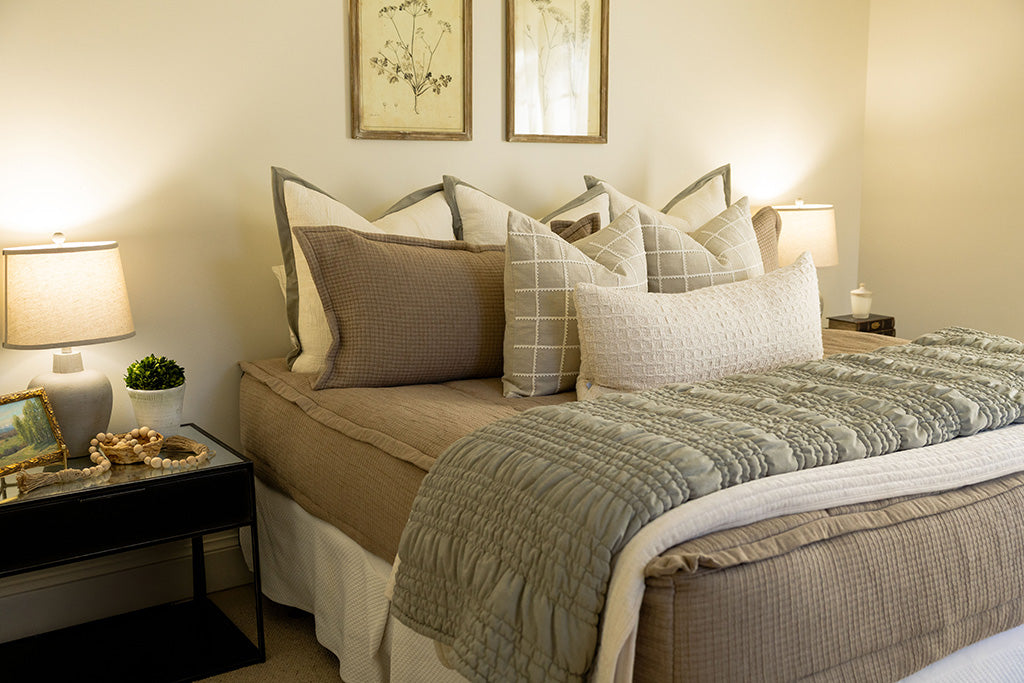 Tan woven quilted bedding with cream and green accessories. 
