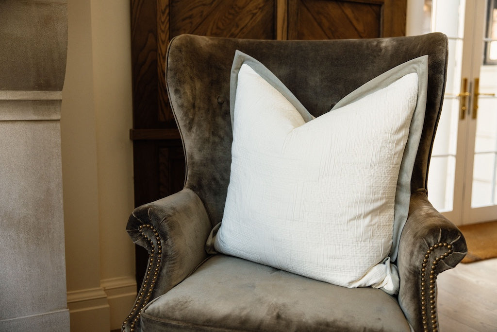 A cream textured and green velvet trim XL pillow on an olive green velvet chair.