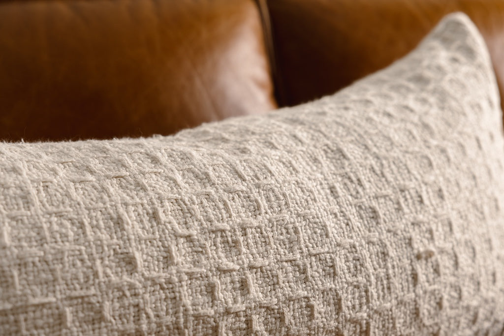 A cream woven XL lumbar pillow on a leather couch.
